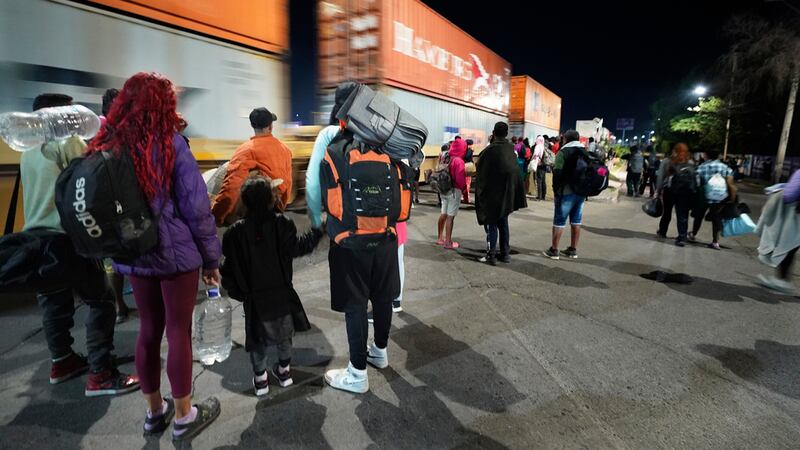 Migrantes miran un tren de mercancías mientras esperan a un tren rumbo al norte que se detenga...